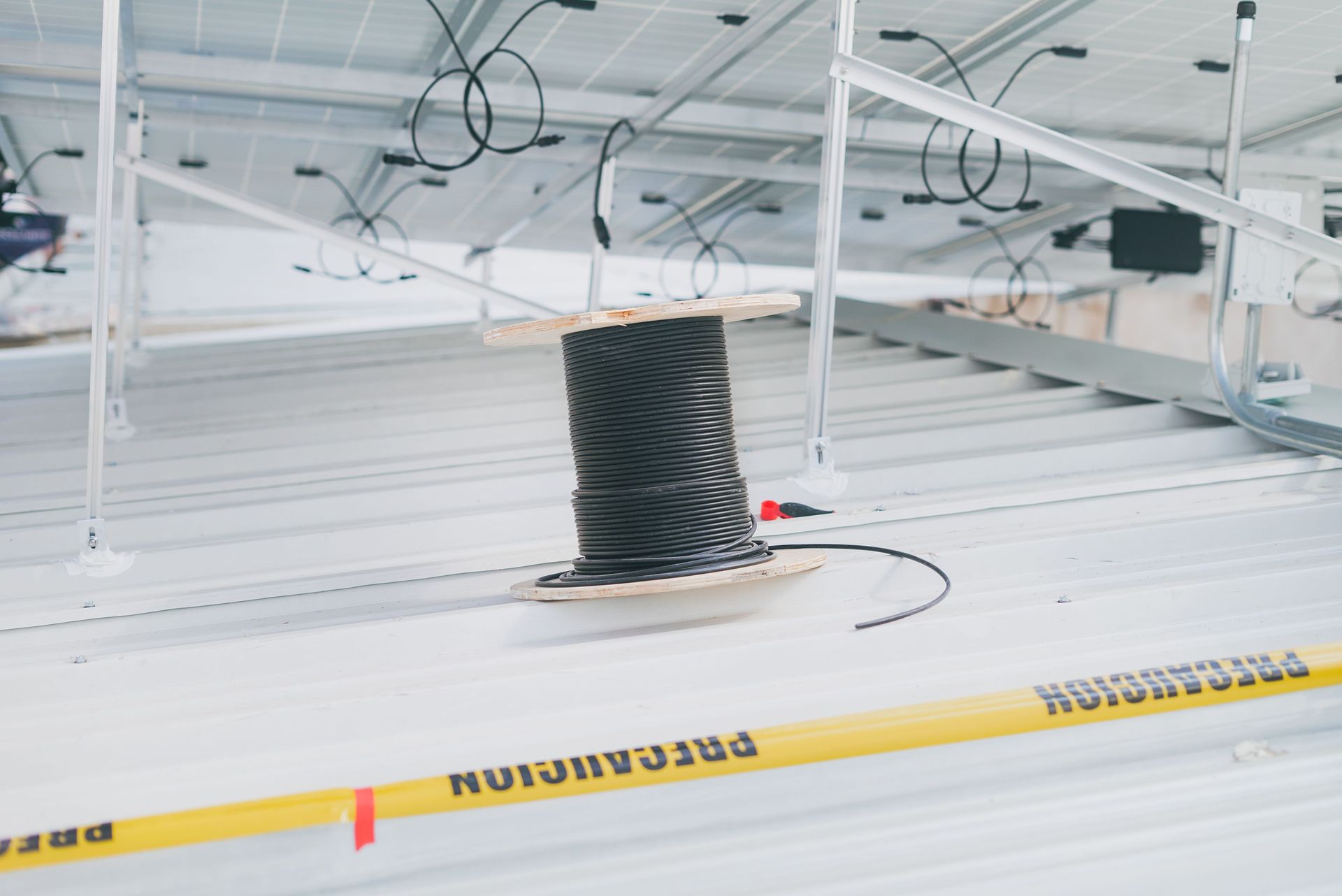 Industrial ceiling with white metal panels, black duct opening, and yellow caution tape across the foreground