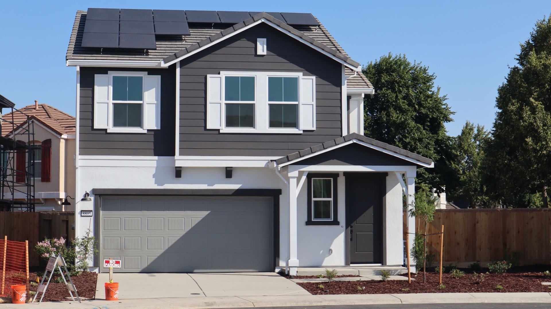 Two-story gray house with solar panels, white trim, and a double garage in a suburban neighborhood