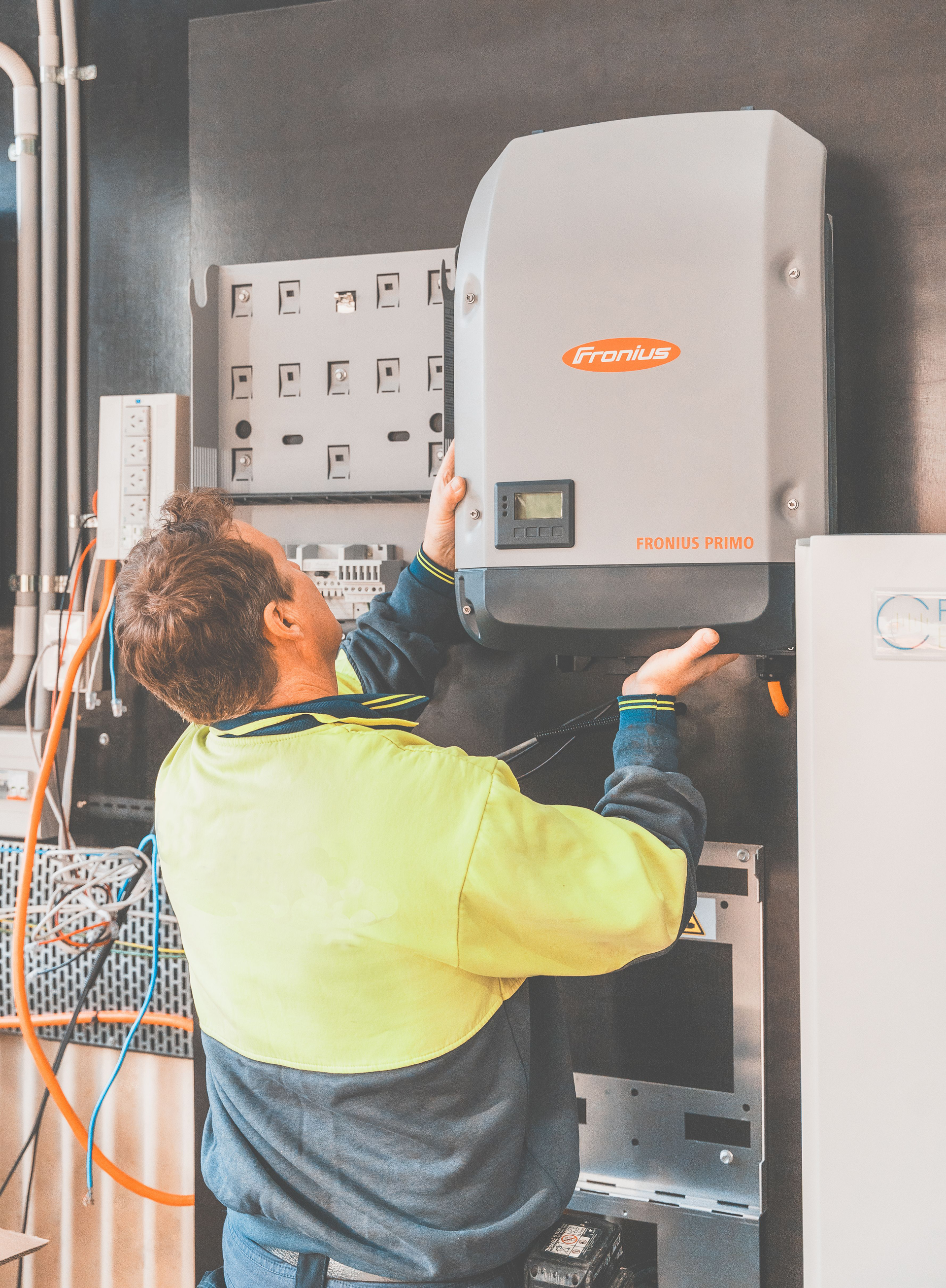 Worker in a high-visibility jacket inspecting a wall-mounted electrical control unit with cables nearby