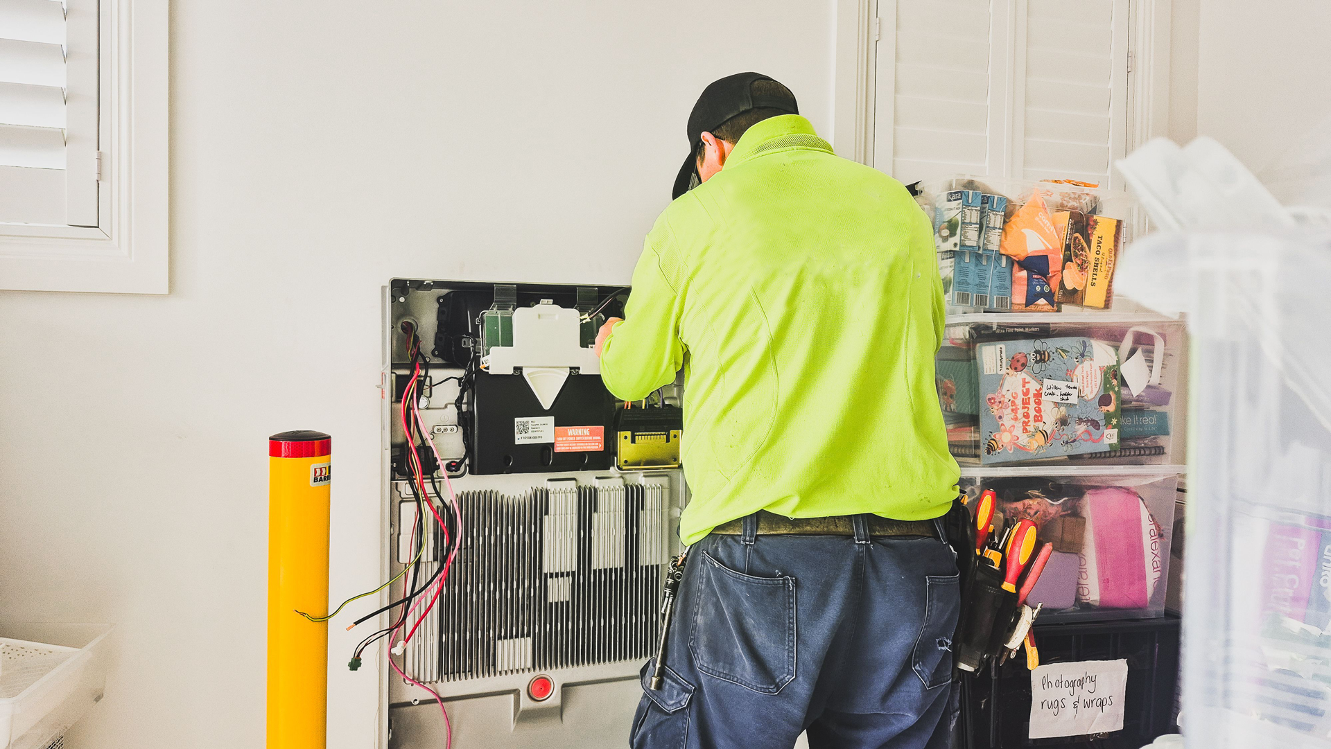 Person in a neon green jacket working at an open cabinet in a room with shelves and supplies