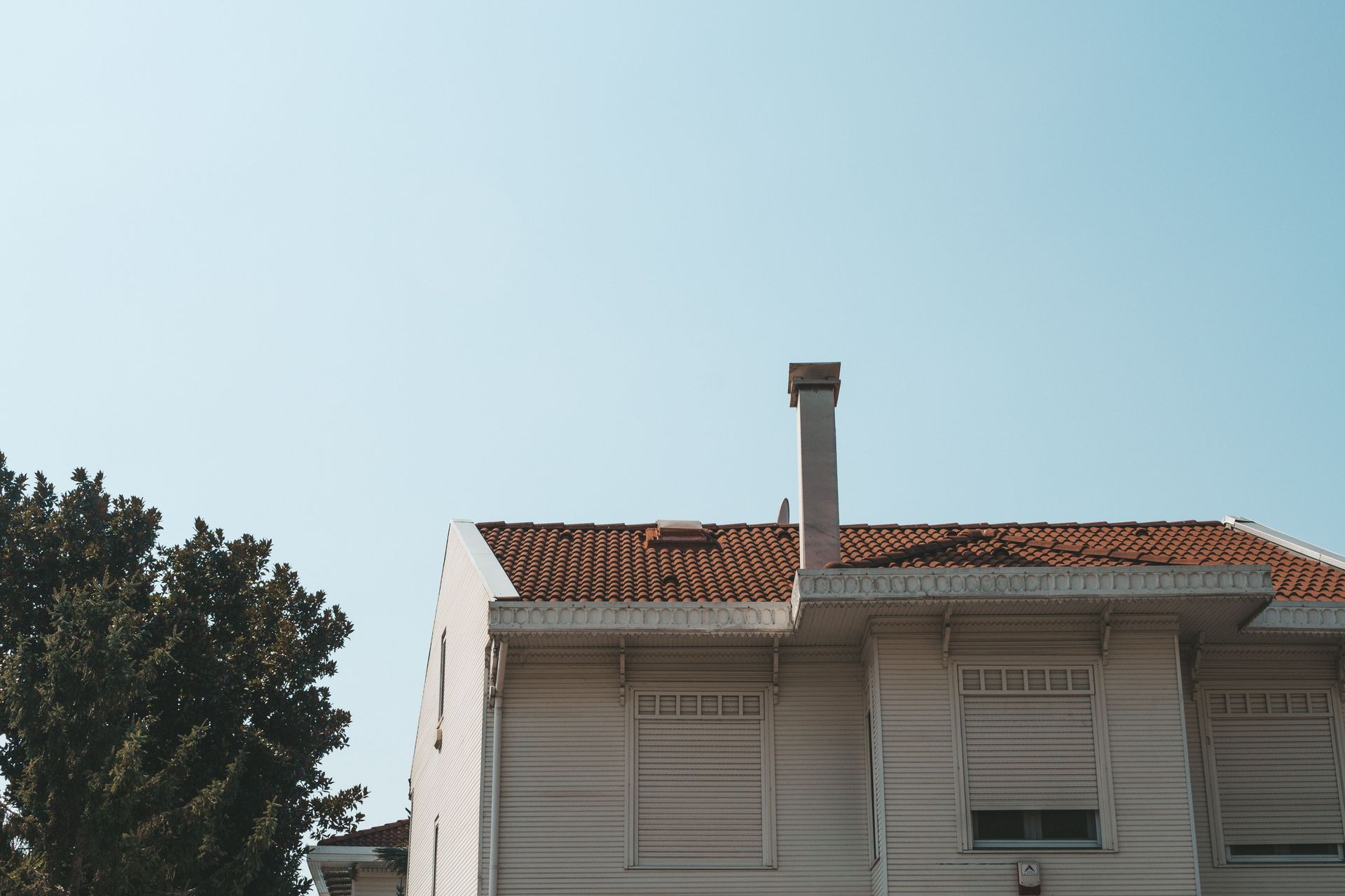 White house roof with red tiles and chimney beneath a clear blue sky