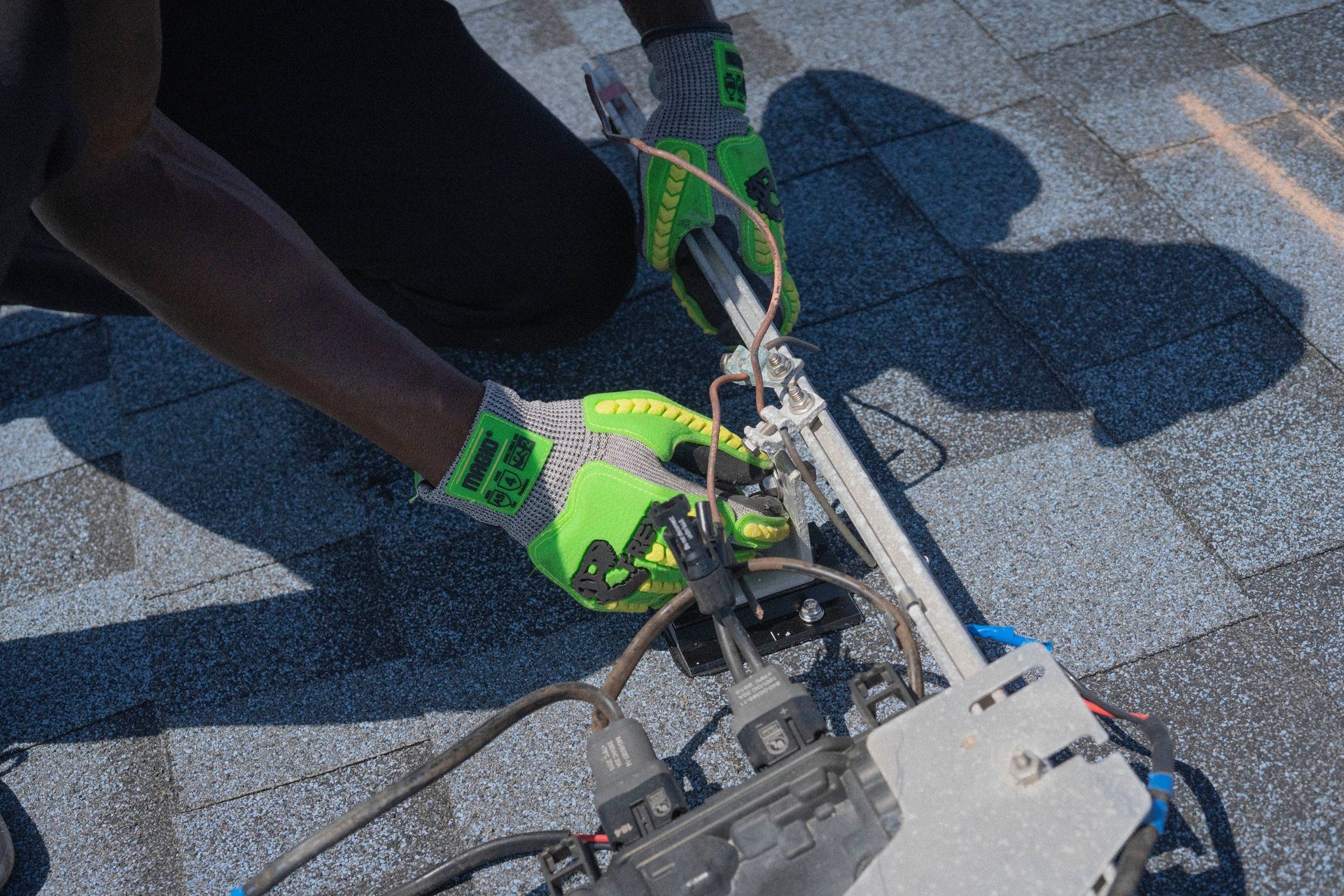 Person working with neon green gloves on rooftop equipment under bright sunlight