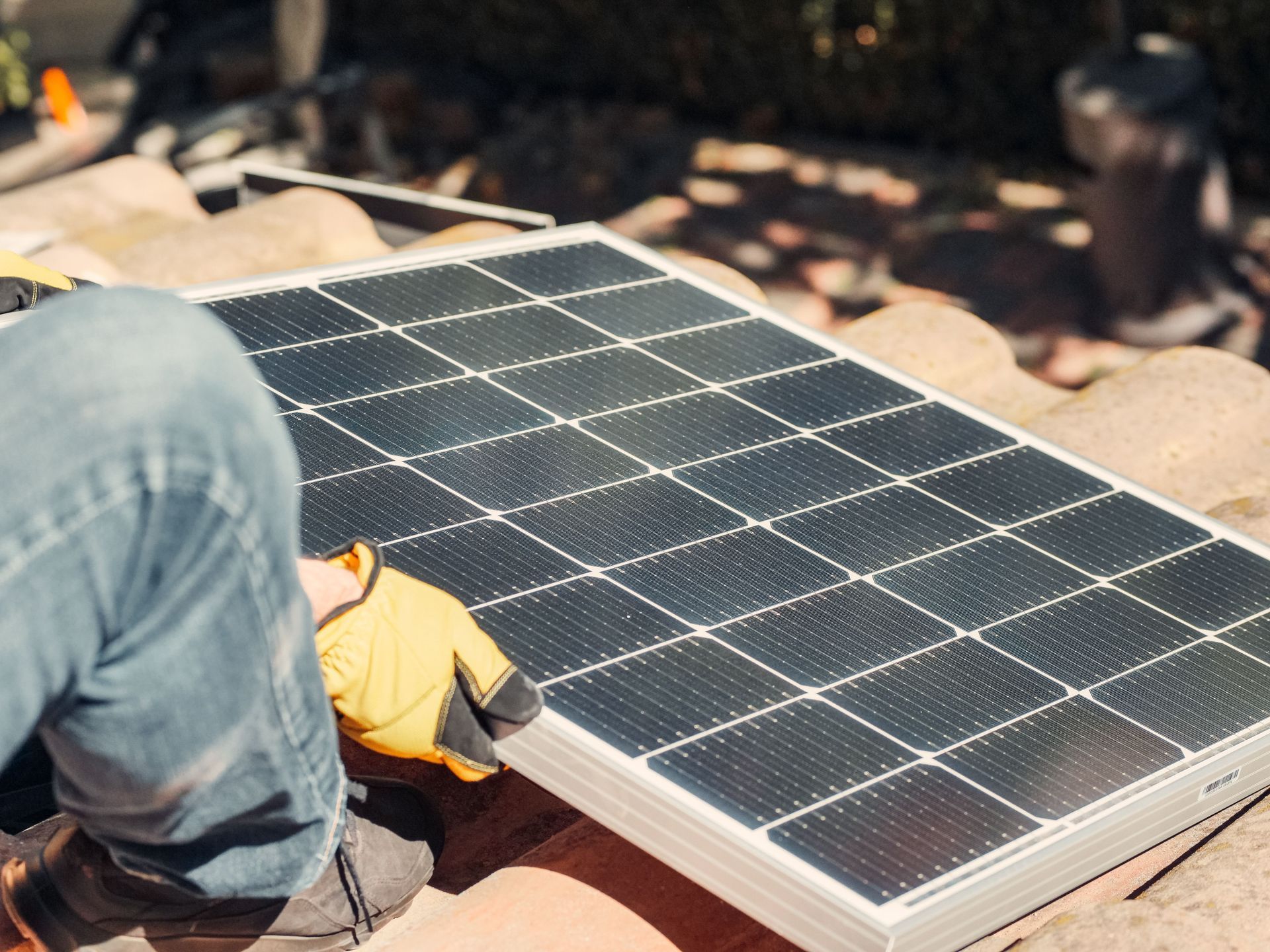 Solar panel being installed outdoors by a worker in yellow gloves and jeans