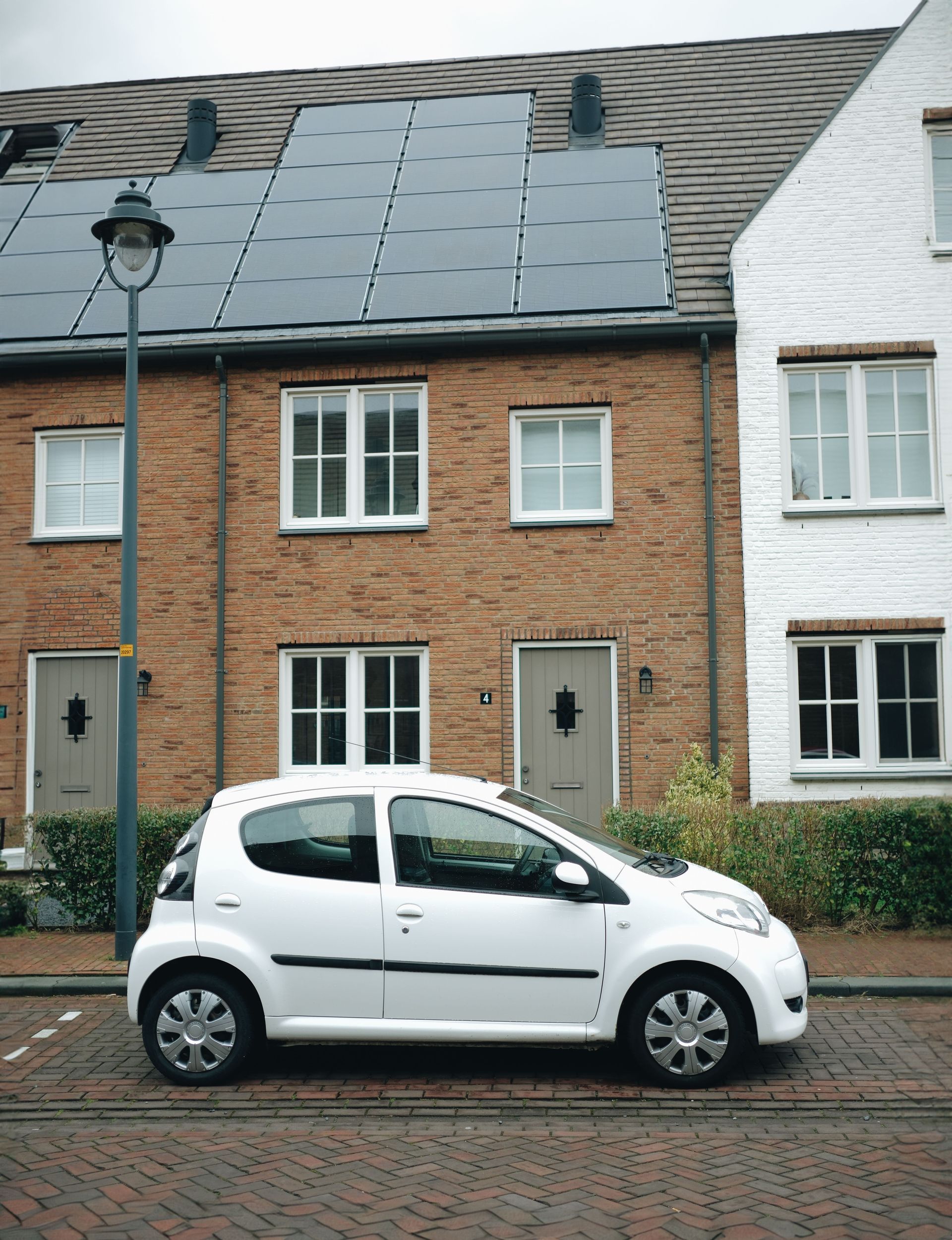 White compact car parked on a brick street in front of a brick townhouse with solar panels on the roof