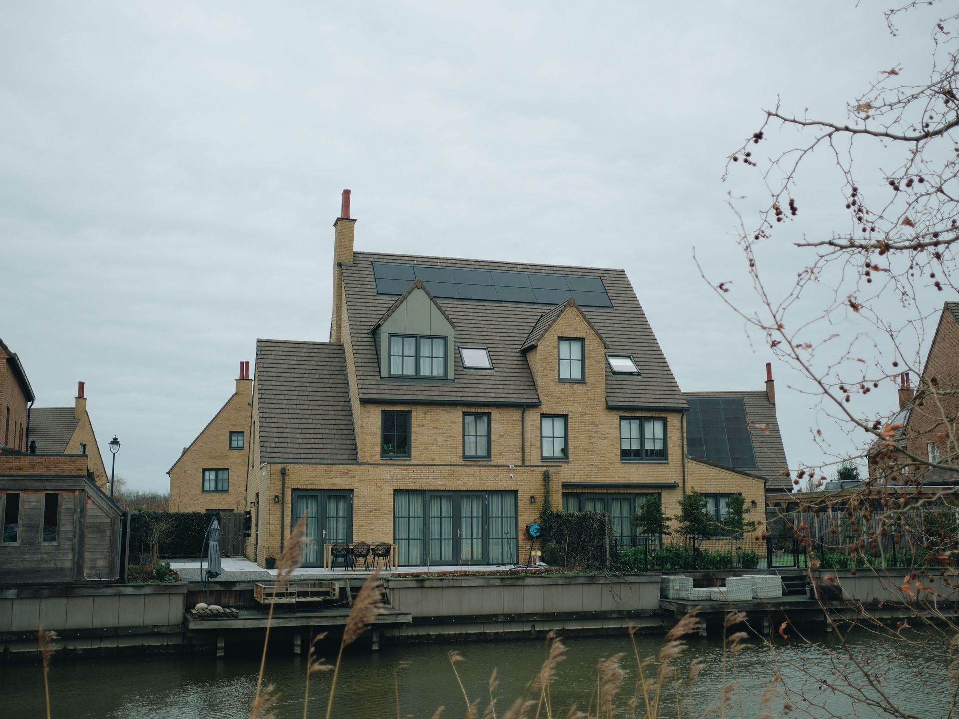Canal-side stone house with gray roof and large windows on a cloudy day