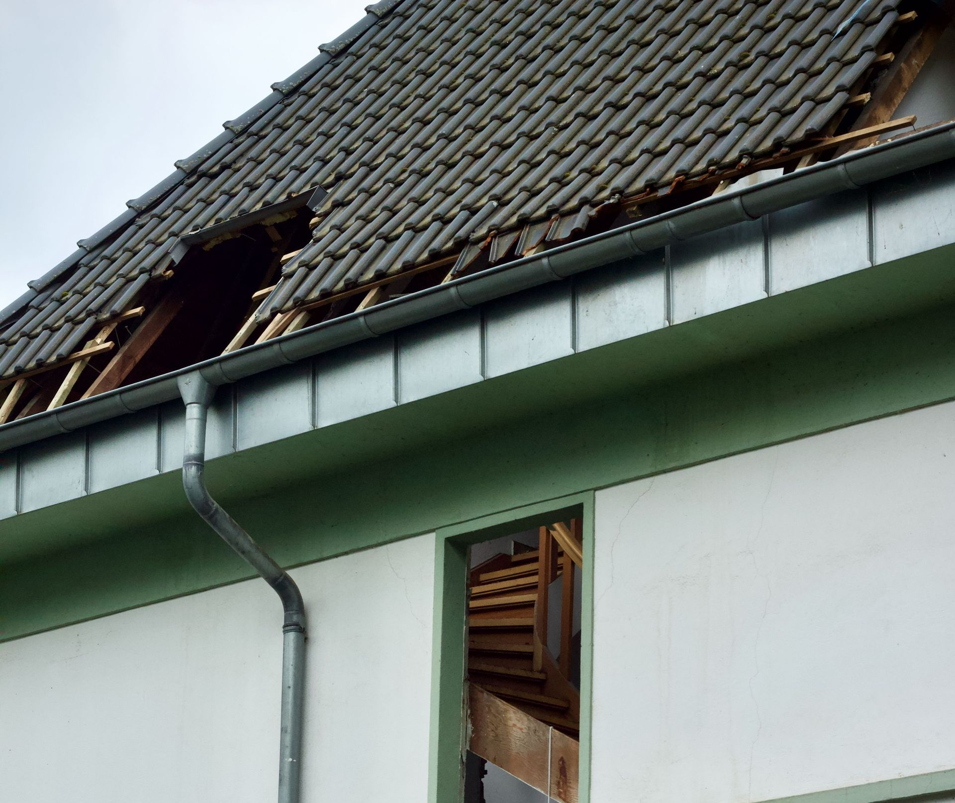 Damaged roof with missing tiles and a broken dormer window on a house