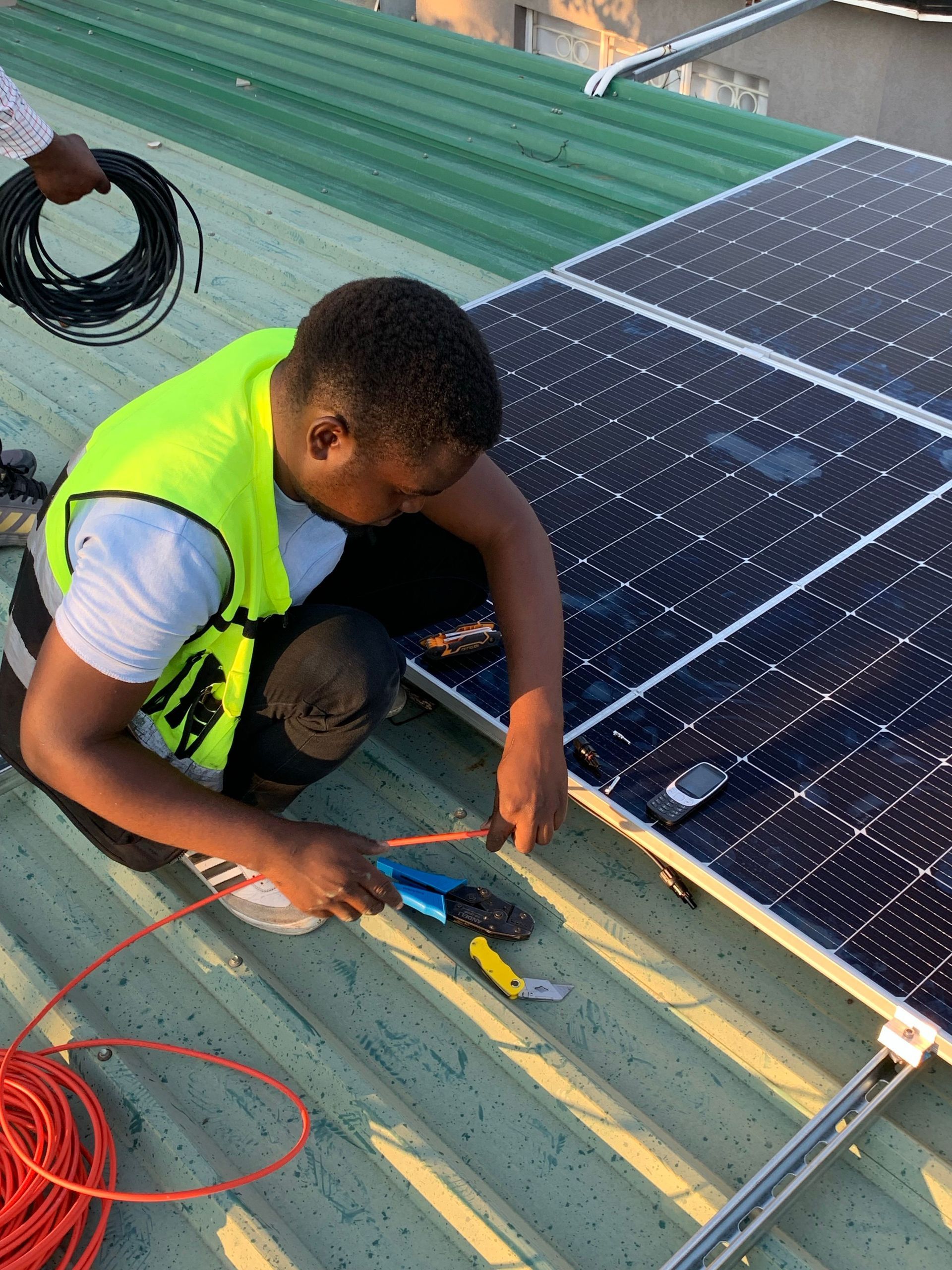 Worker in a safety vest installing solar panels on a metal rooftop using hand tools.