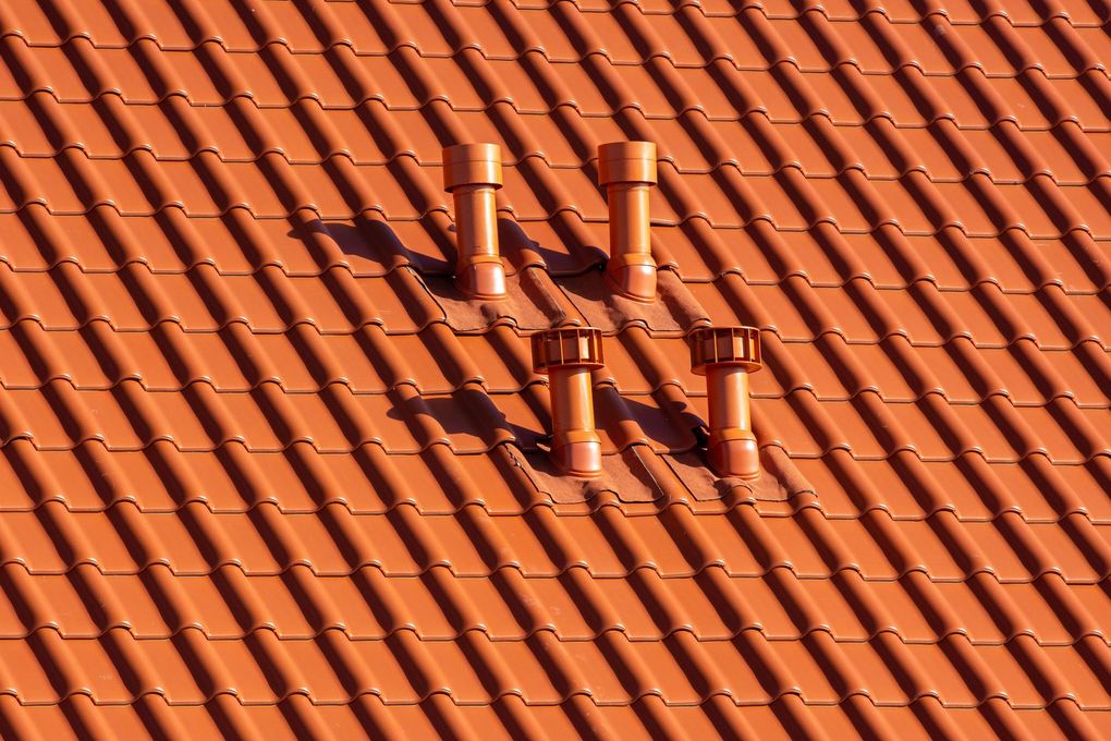 Red clay tile roof with four small chimneys and strong diagonal sunlight shadows
