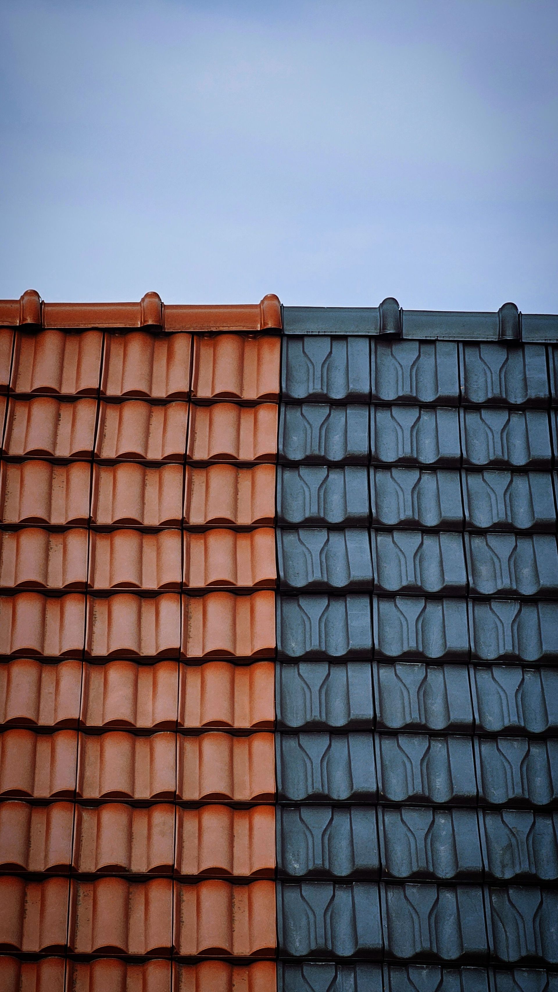 Split view of a tiled roof, with terracotta tiles on the left and dark blue-gray tiles on the right.