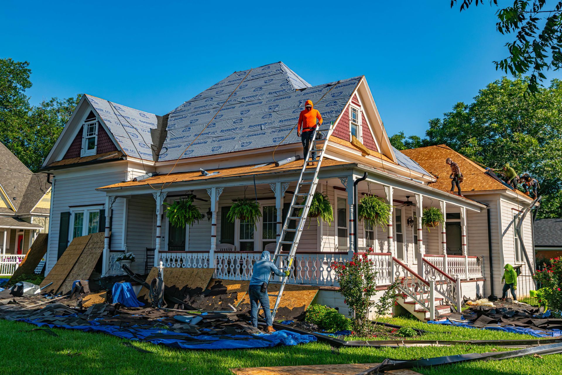 Workers repairing the roof and porch of a white house on a sunny day