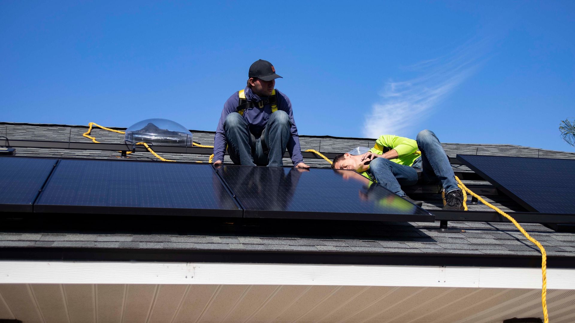 Two workers installing solar panels on a rooftop under a clear blue sky