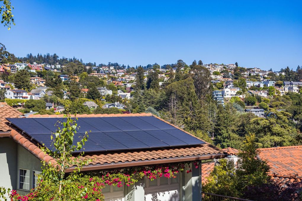 Rooftop solar panels overlooking a sunny hillside neighborhood with trees and houses