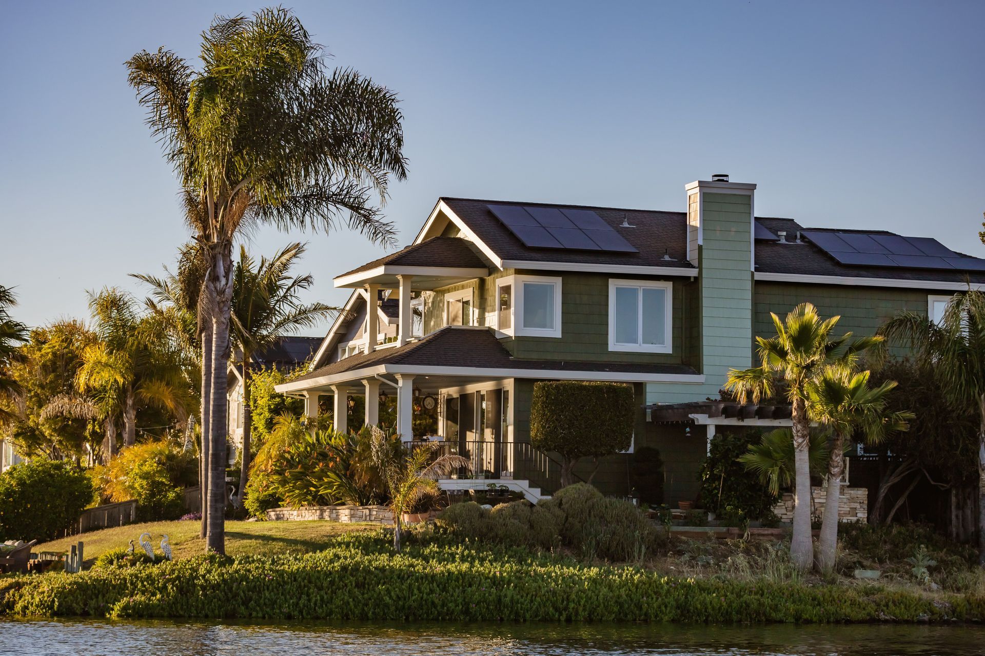 Two-story house with a front porch, palm trees, and solar panels in a sunny neighborhood