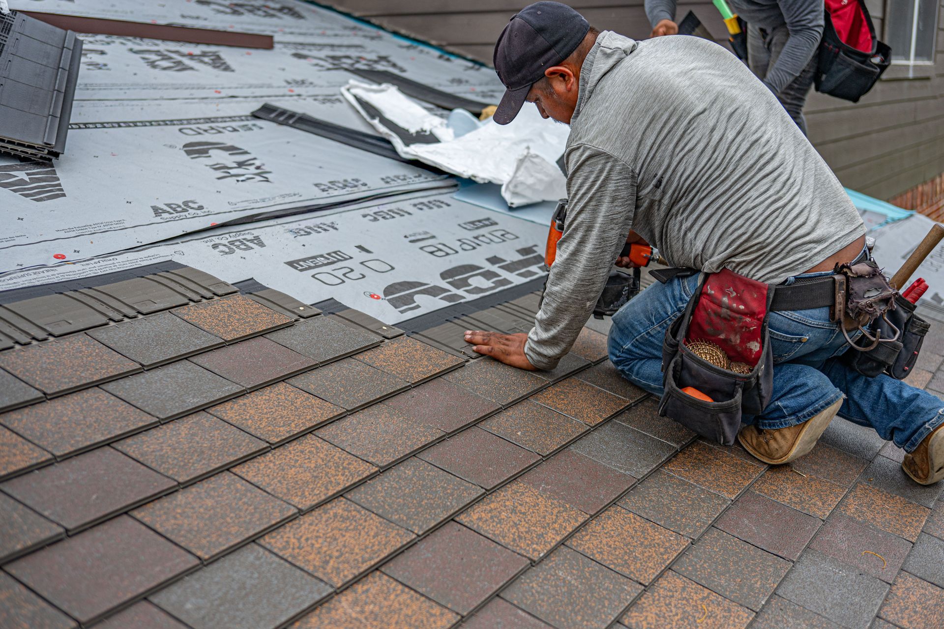Worker installing roof shingles beside black underlayment and brown tiles