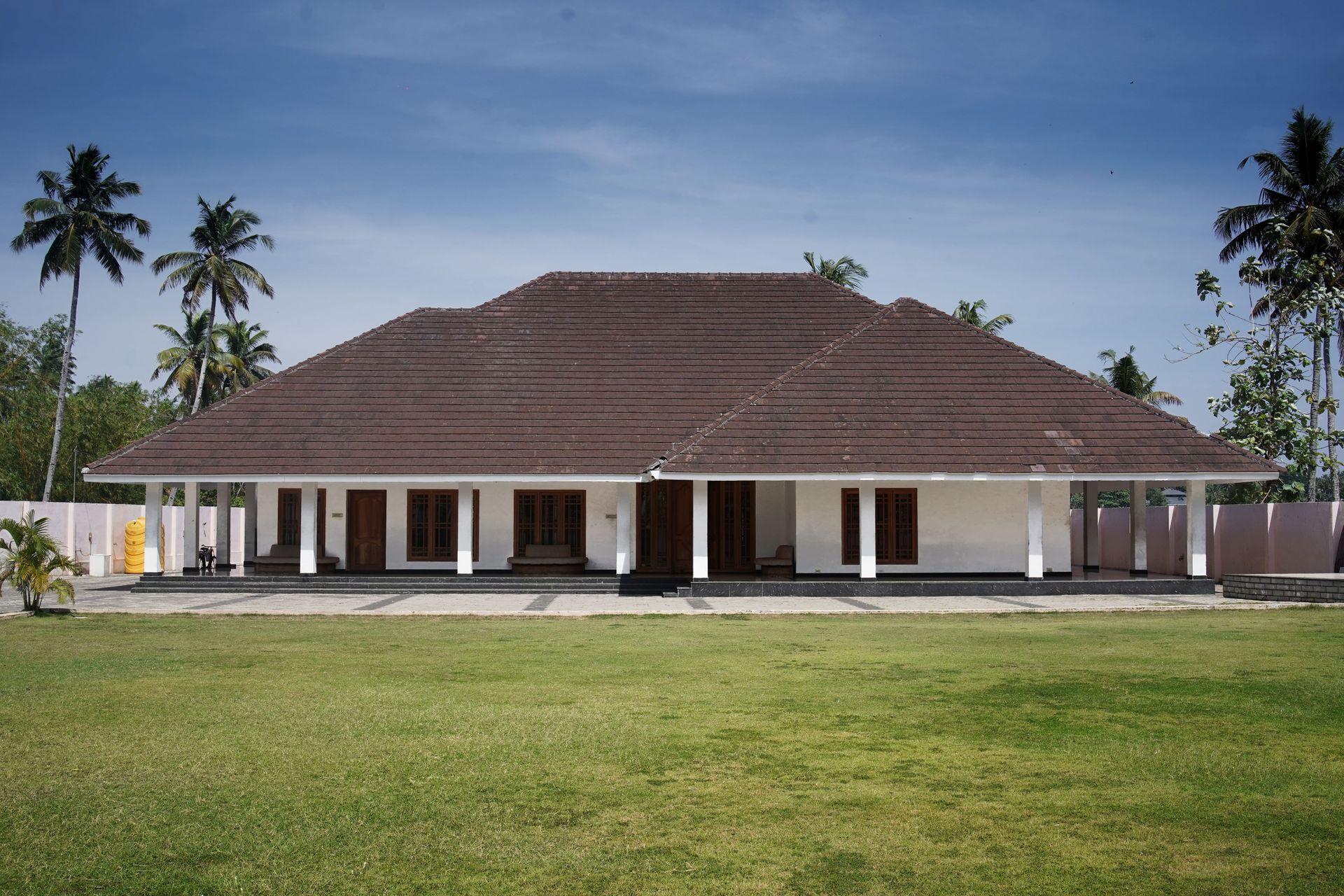 Low, white colonial-style building with a brown roof, surrounded by palm trees and green lawn