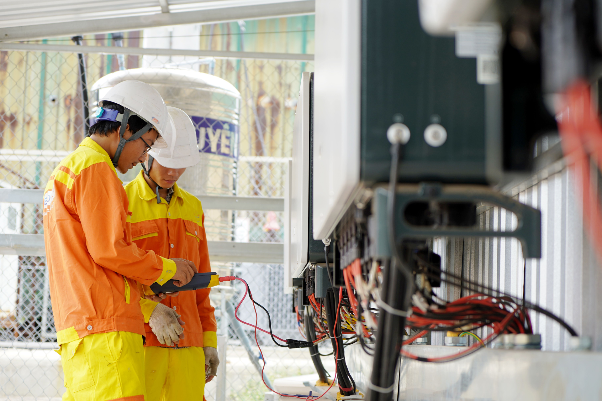Two workers in safety gear inspect cables in an industrial facility