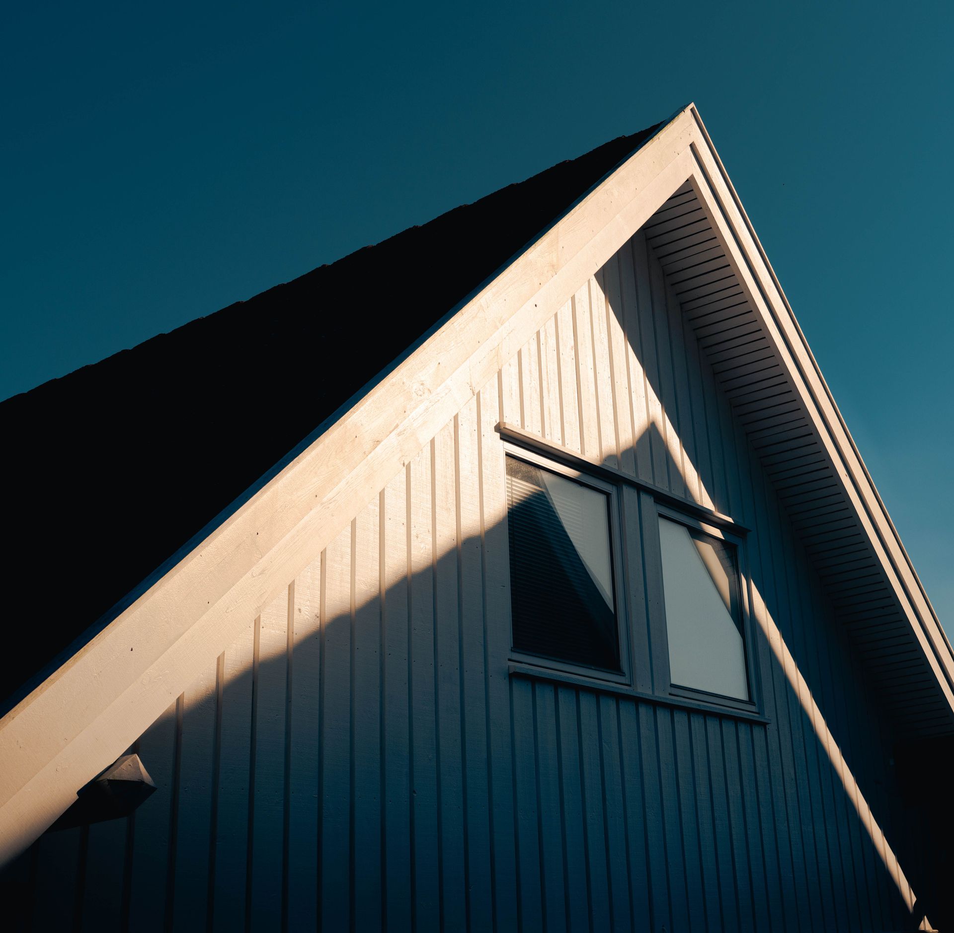 White house gable with a window against a deep blue sky, lit by warm sunlight