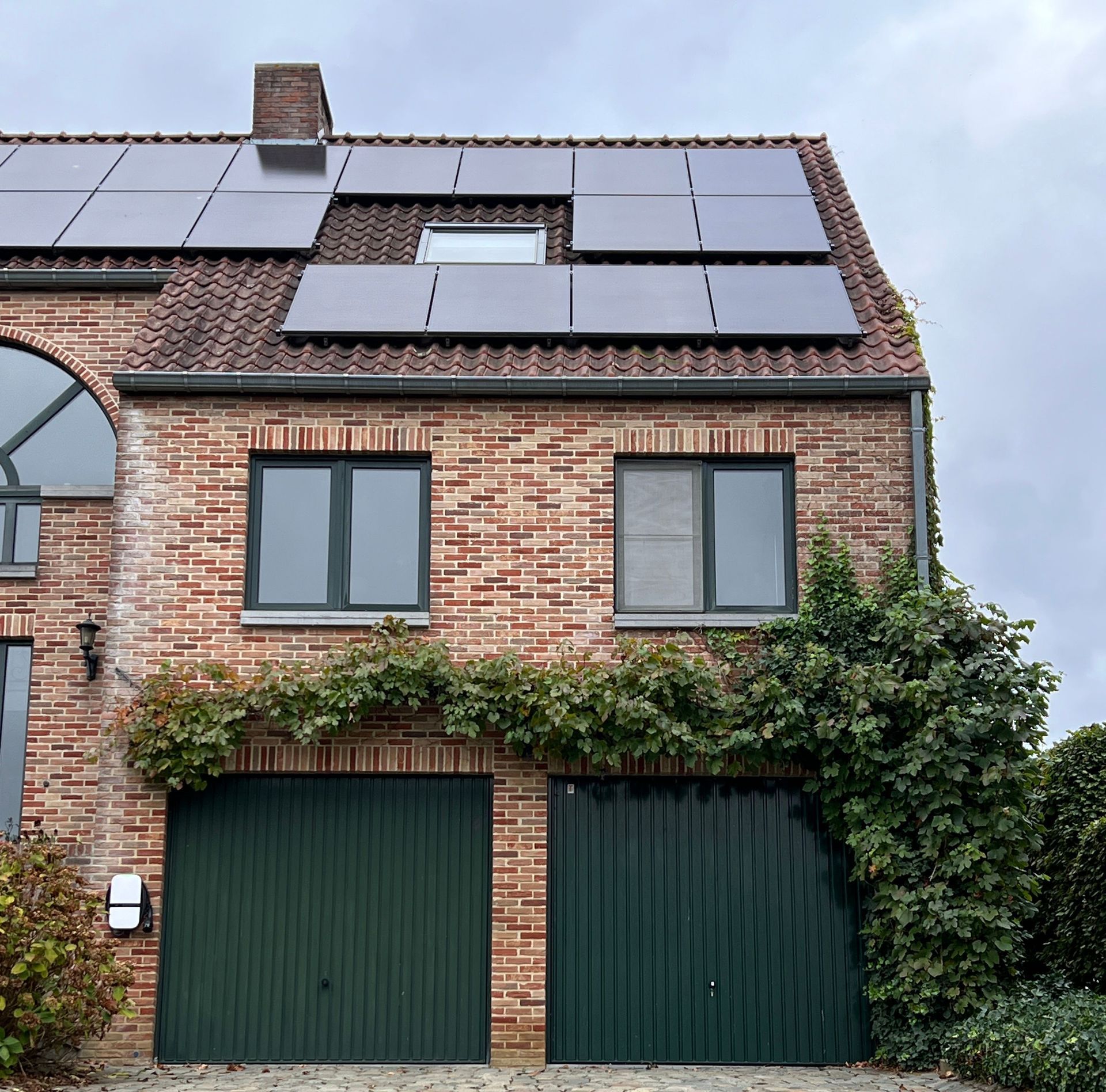 Brick townhouse with solar panels, green garage doors, and ivy climbing the front facade