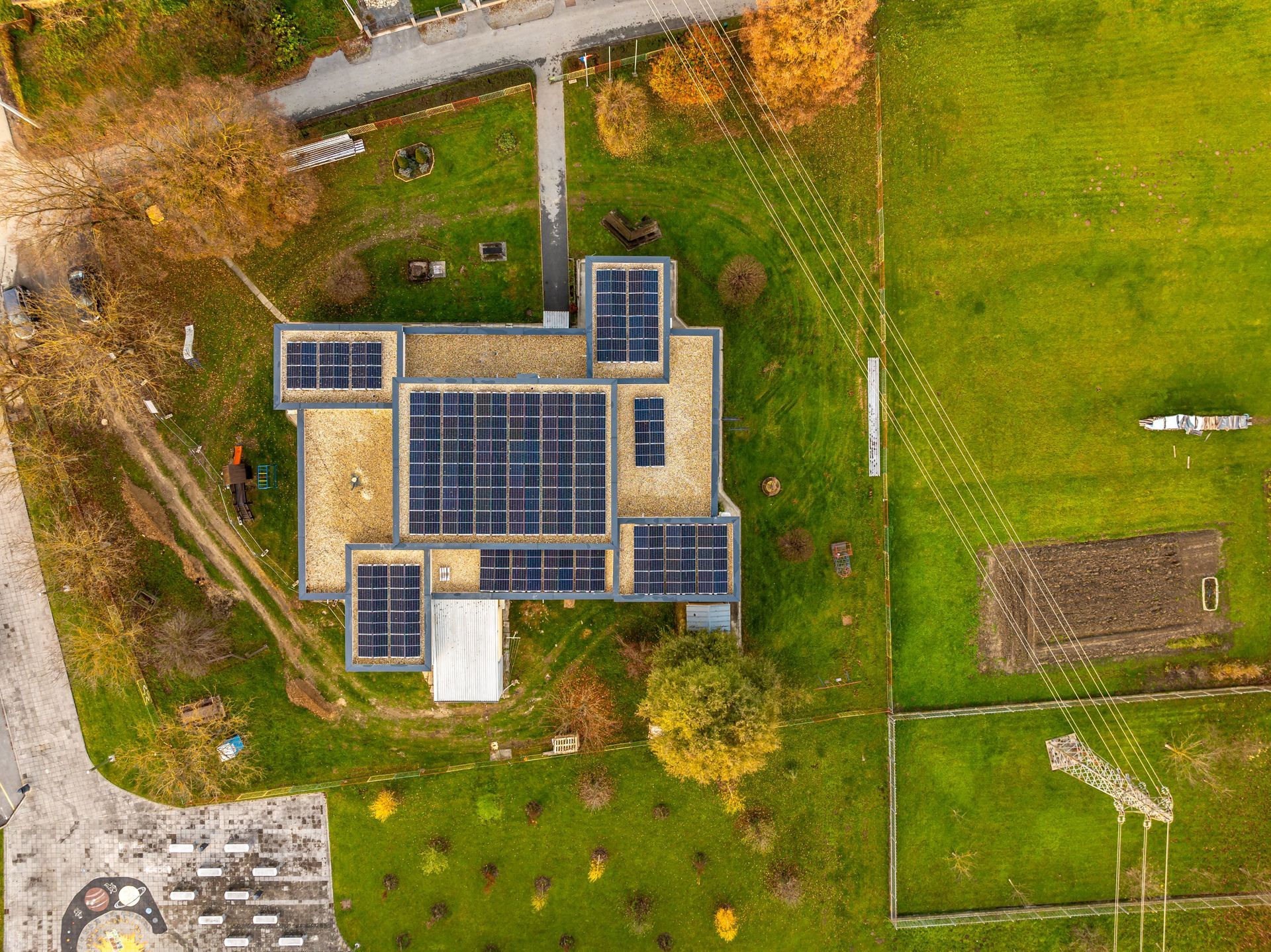 Aerial view of a house with rooftop solar panels beside green fields and paths