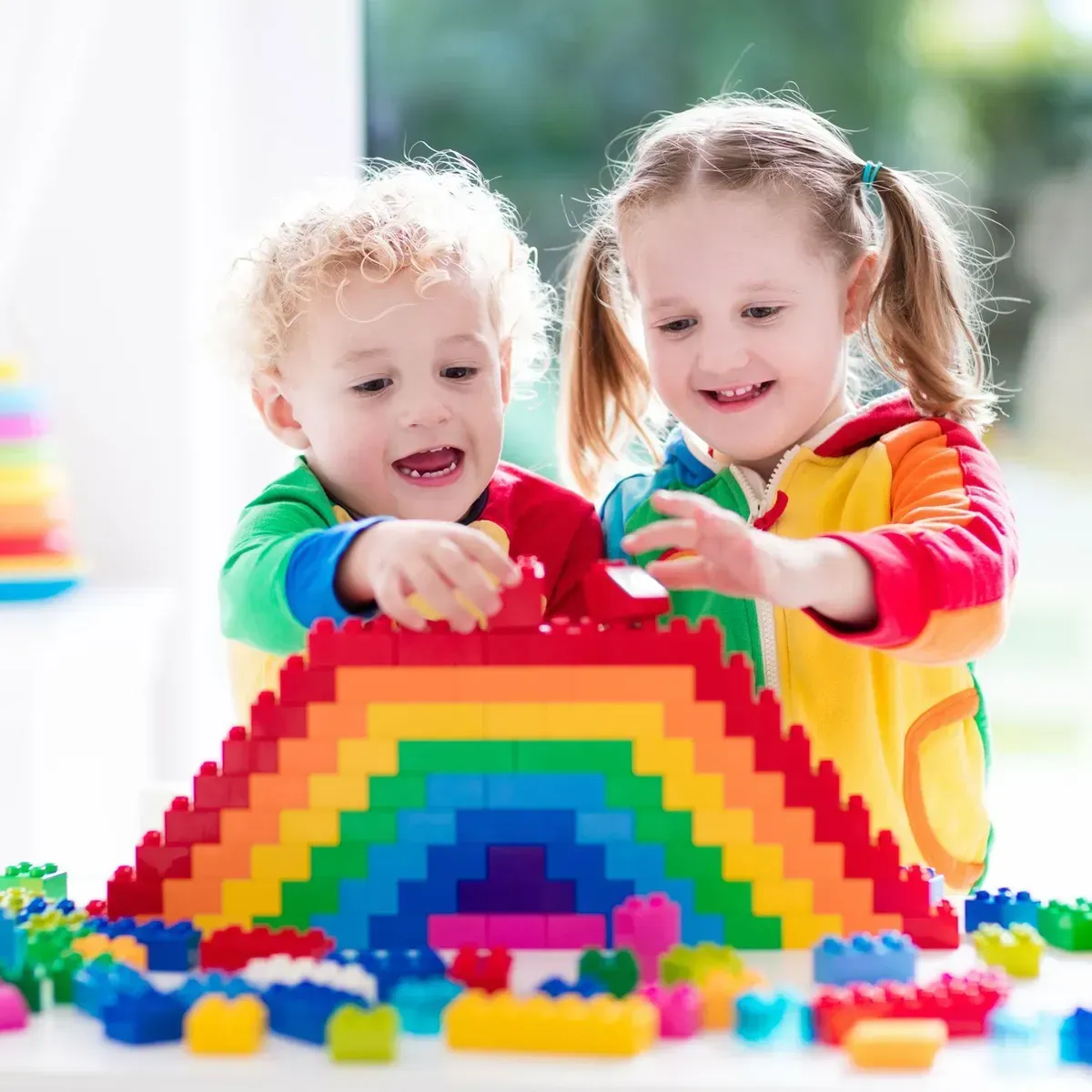 Two children building a colorful rainbow block arch together at a table