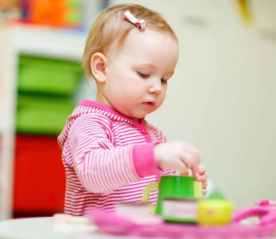Toddler in a pink striped shirt playing with colorful toy blocks on a table