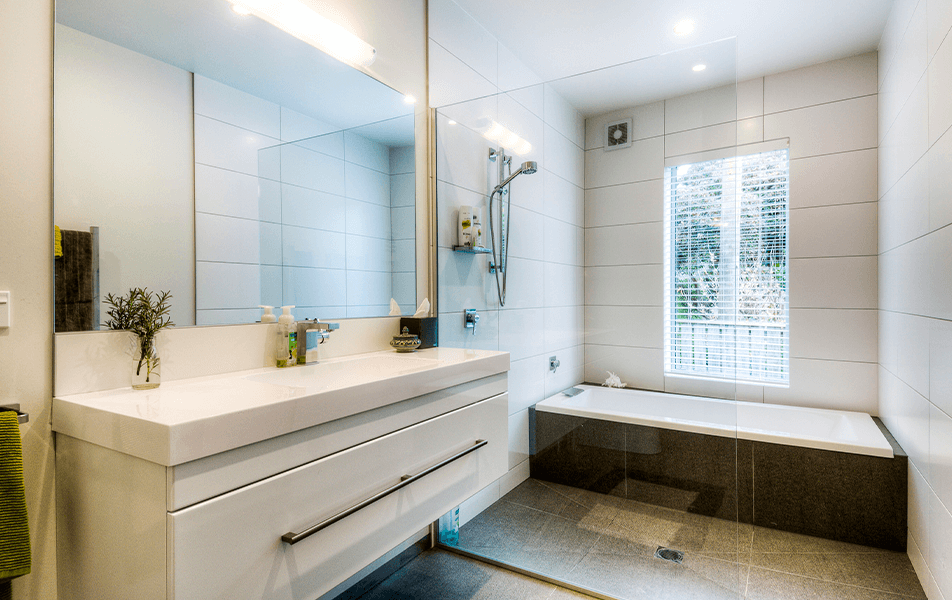 Modern bathroom with white tile, large mirror, vanity, and a bathtub near a window.