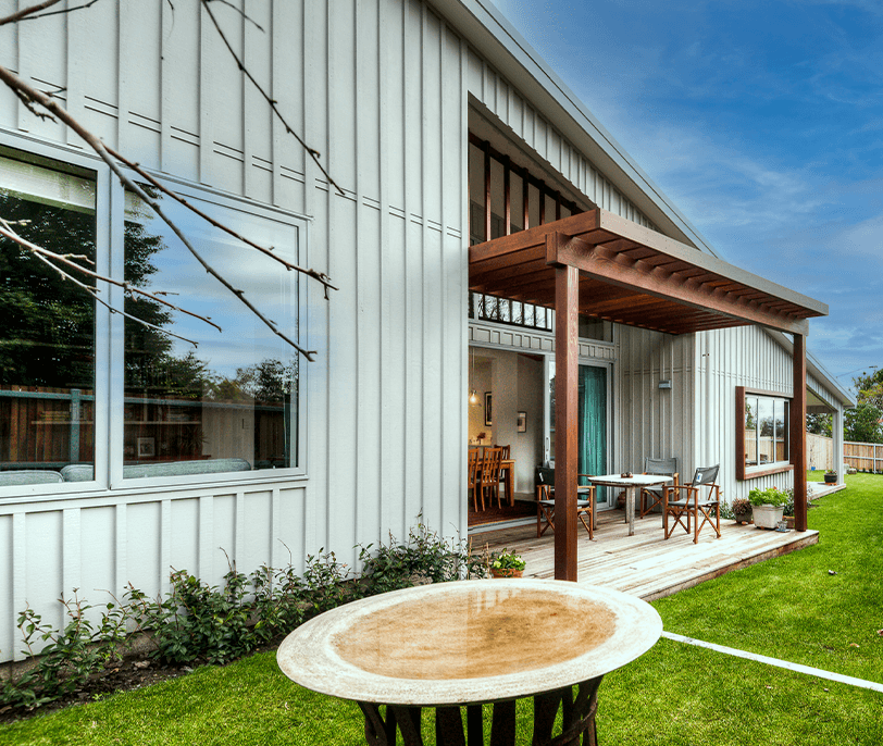 Modern home exterior with covered patio, wood pergola, and lush green lawn.