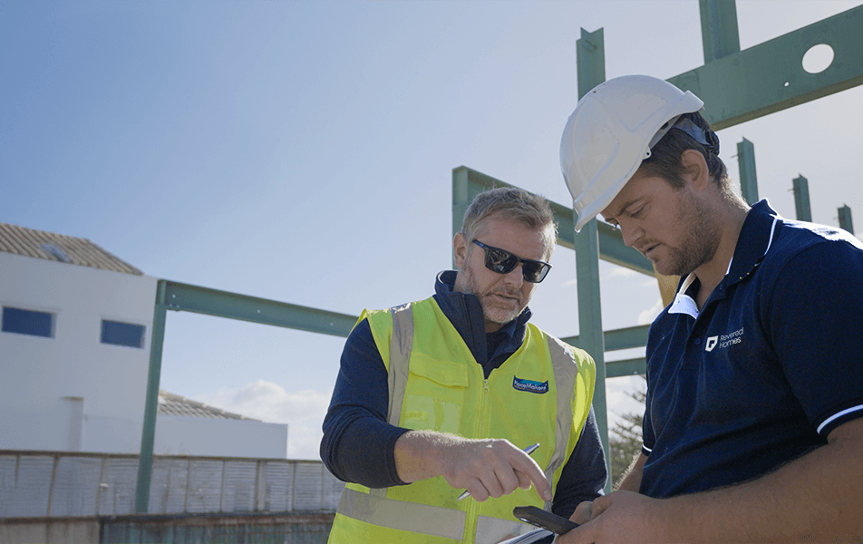 Two men, one in a hard hat, reviewing plans at a construction site under a bright blue sky.