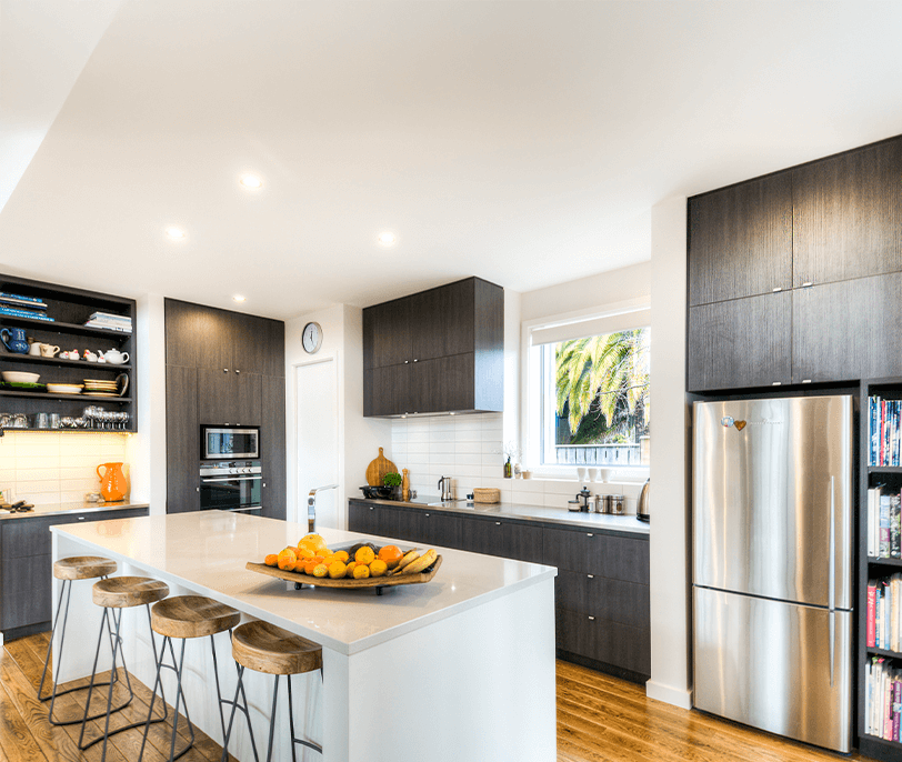 Modern kitchen with dark wood cabinets, stainless steel fridge, white island, and wooden stools.