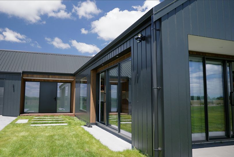 Terracotta-colored modern house with large windows, concrete patio, and green lawn.