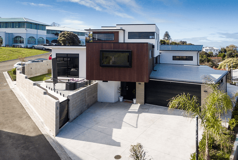 Modern two-story house with dark brown siding, concrete driveway, and black garage door.