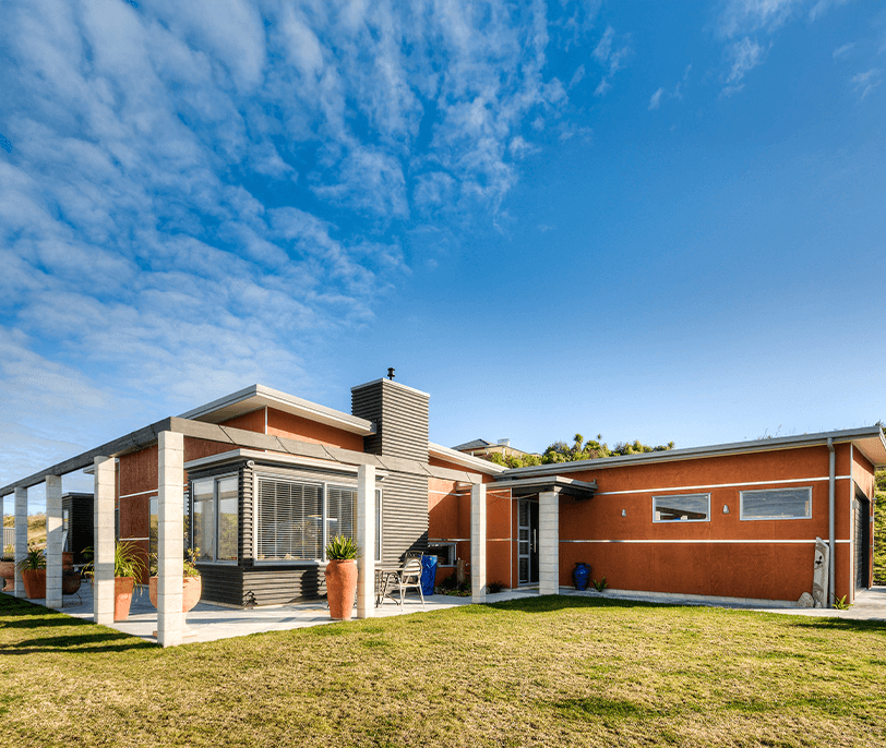 Modern, single-story home with brown stucco siding, green lawn, and blue sky.