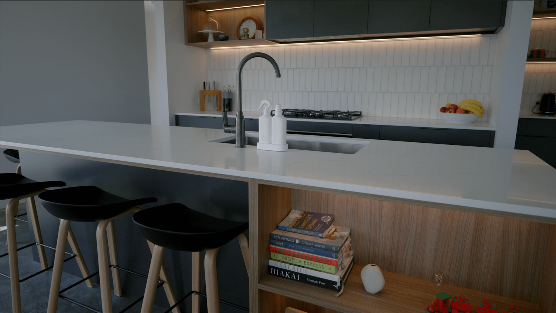 Modern white kitchen with black island, stainless steel appliances, and staircase.