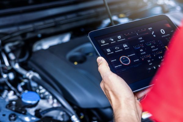 Person holding a tablet displaying vehicle diagnostics next to an open car engine. The screen shows various data points. | King's Auto Center