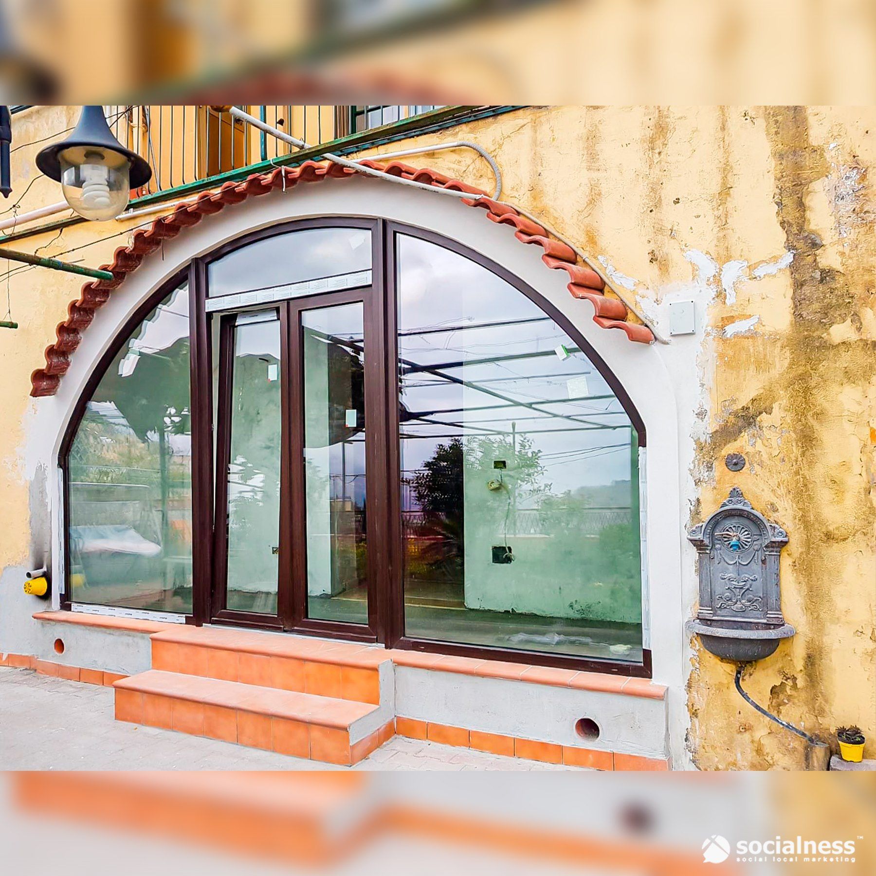 Finestra e porta ad arco con cornice marrone su un edificio giallo. Gradini in piastrelle arancioni conducono all'ingresso.