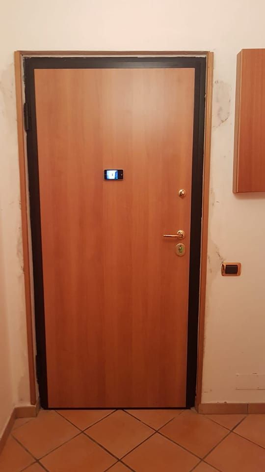 Porta in legno con finiture nere e un piccolo visore digitale, incastonata in una parete bianca.