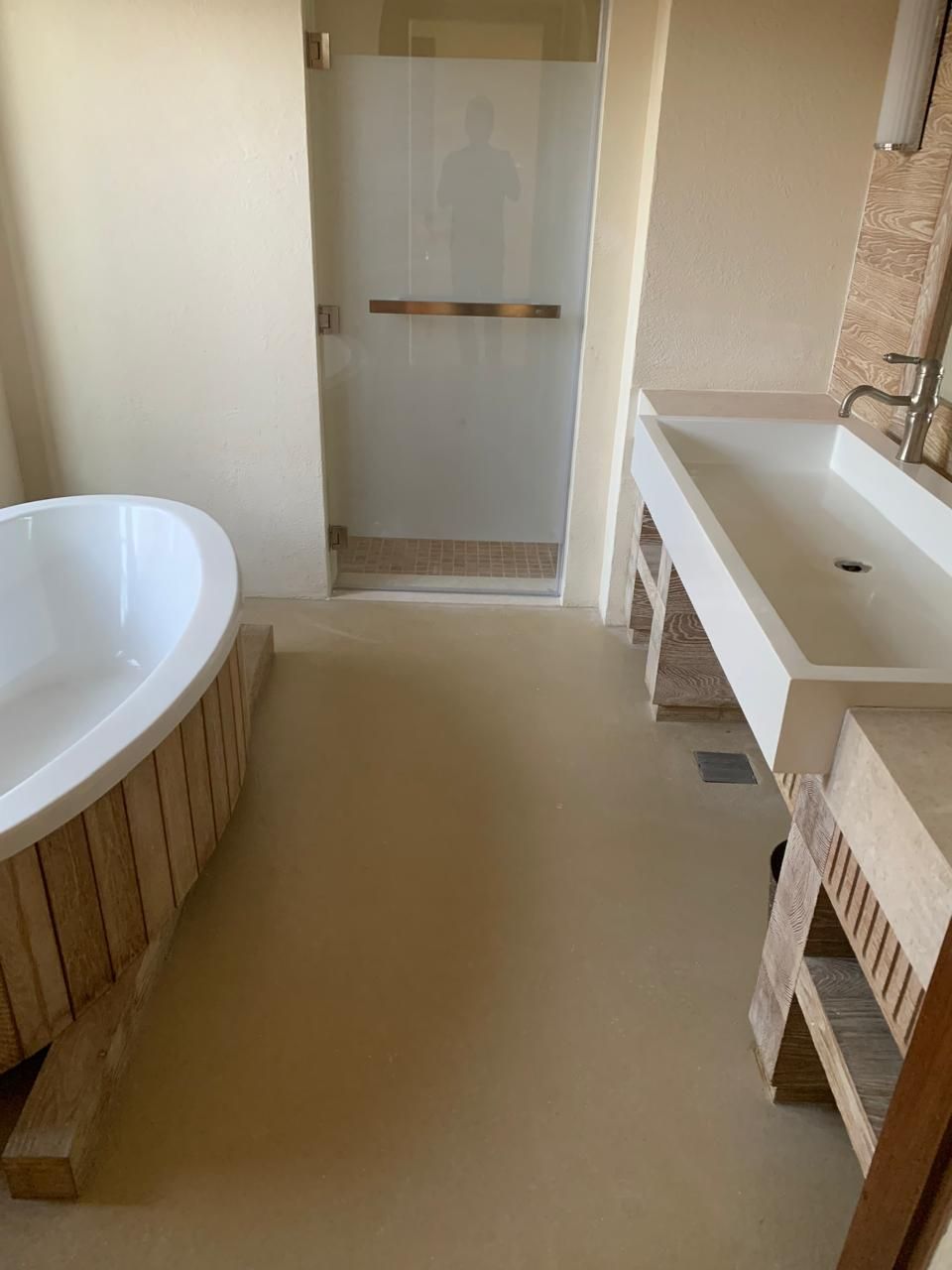 Bathroom with a freestanding bathtub, a glass-doored shower, and a long, trough-style sink. Beige walls and flooring.