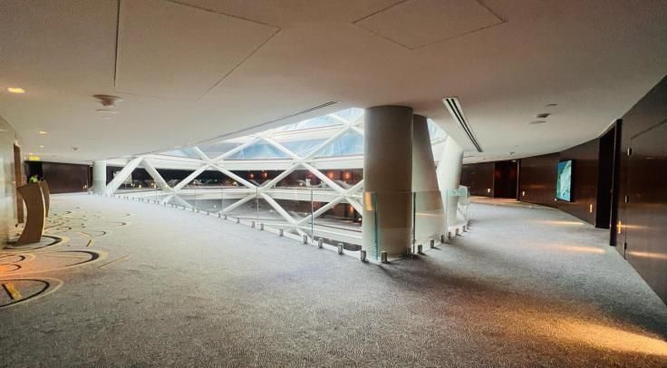 Interior view of a modern, curved hallway with gray carpet, white pillars, and a geometric skylight.