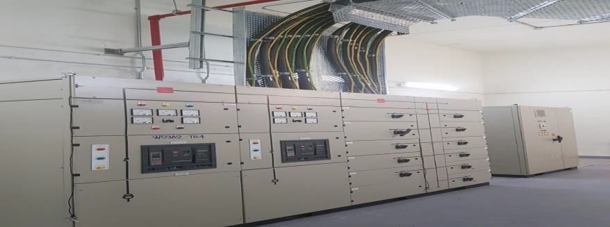 Electrical control panels in a white room with exposed wiring and cabling.