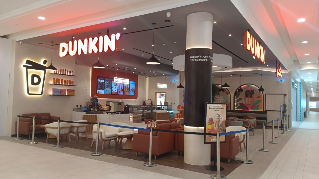 Dunkin' Donuts storefront inside a mall. The shop features orange signage, brown seating, and a menu board.