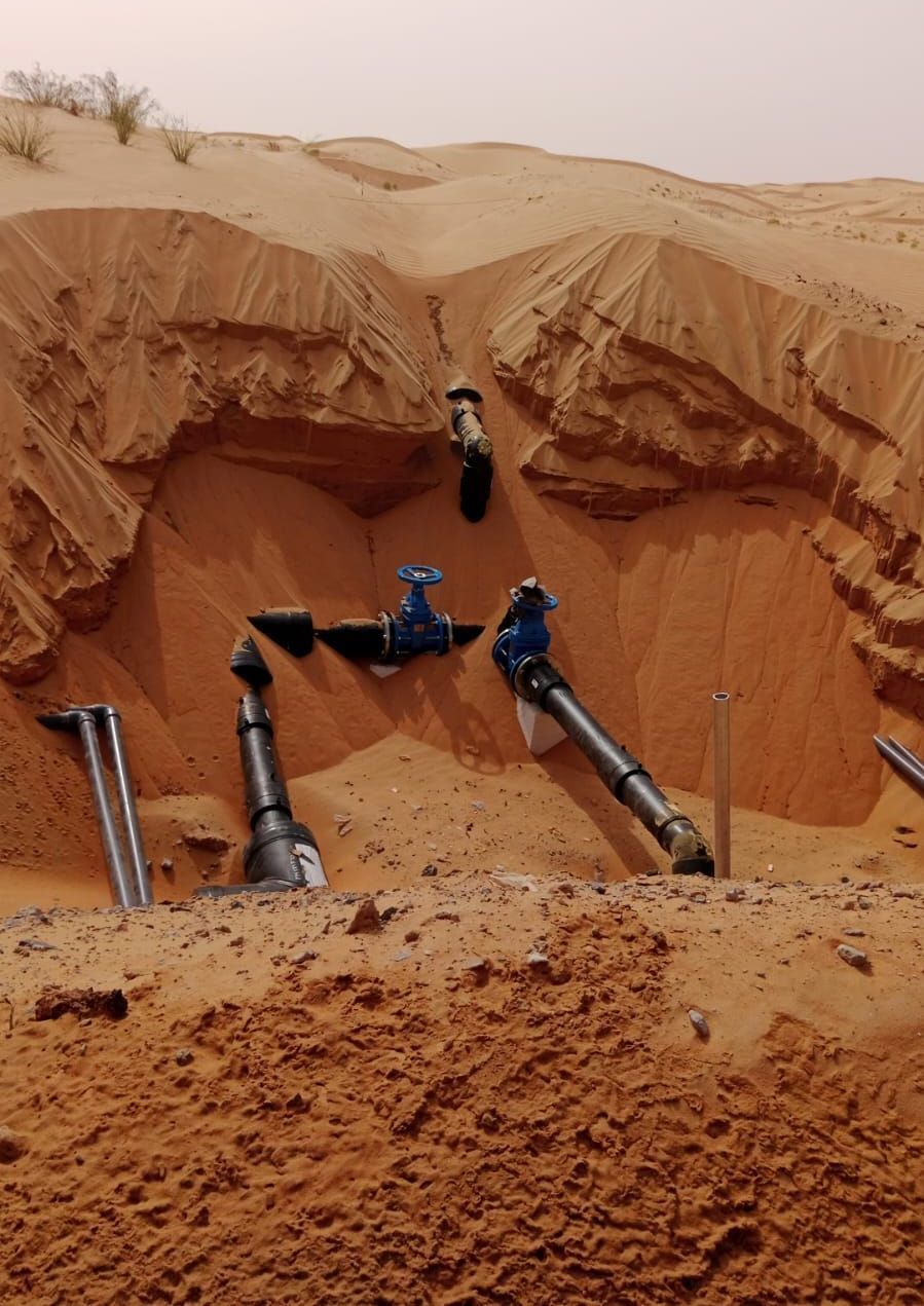 Pipes and valves exposed in a sand pit, likely for water access in a desert environment.