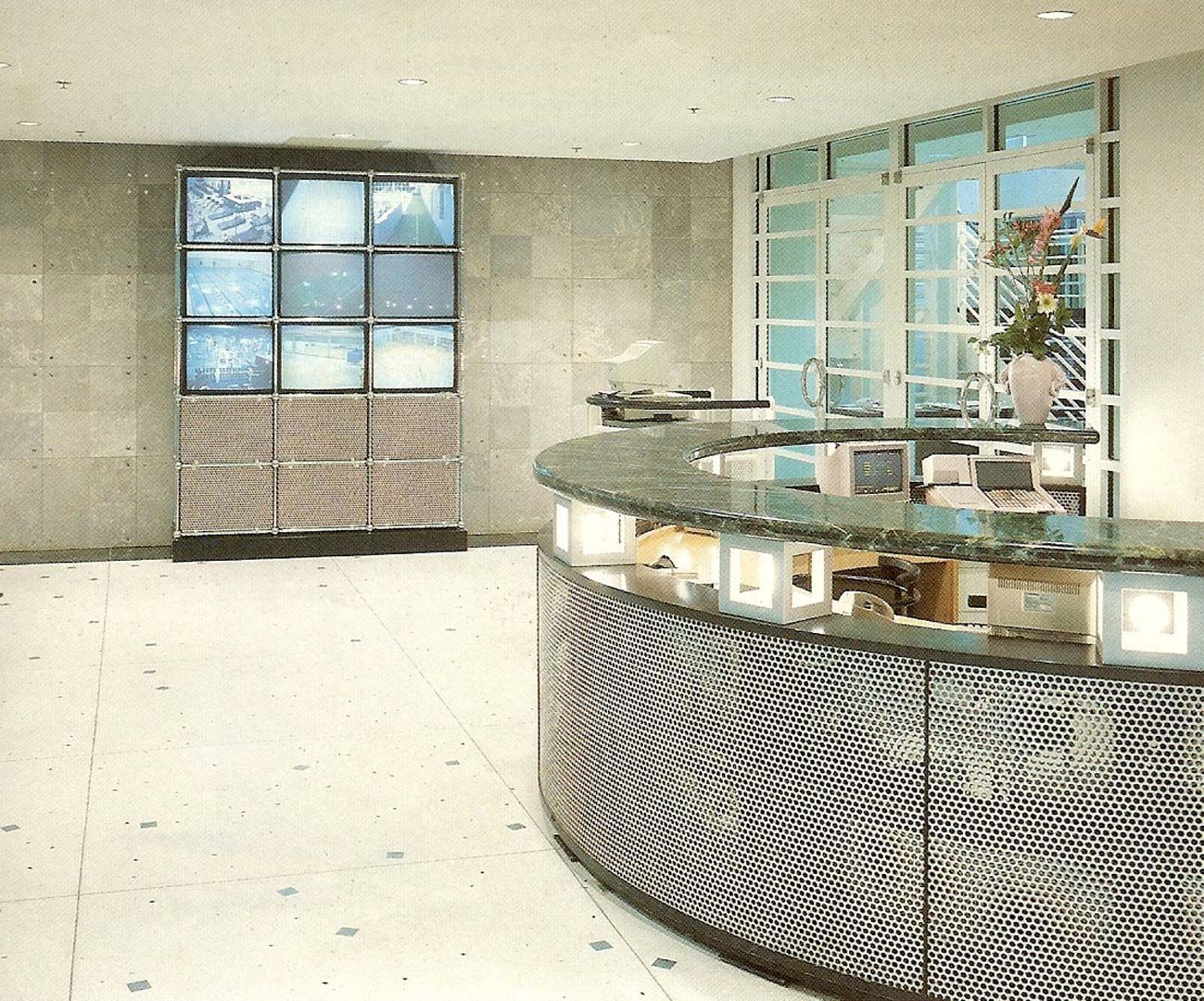 Reception area with a curved counter and a stacked grid of televisions; white walls and floor.