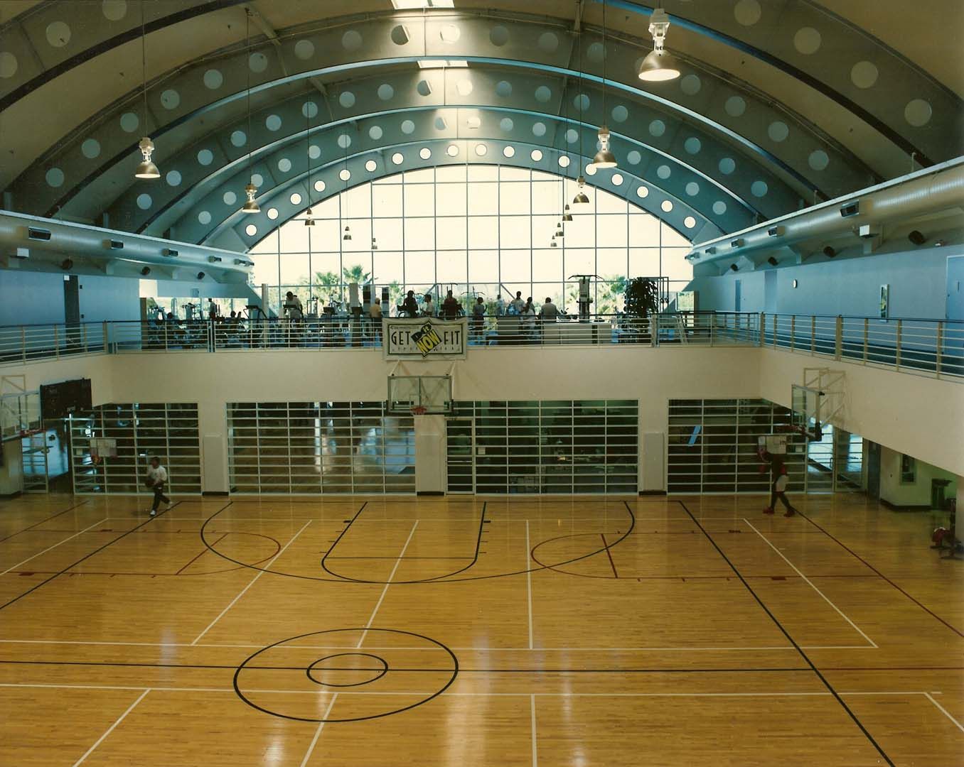 Basketball court inside a gymnasium with a high arched ceiling and a balcony overlooking the court.