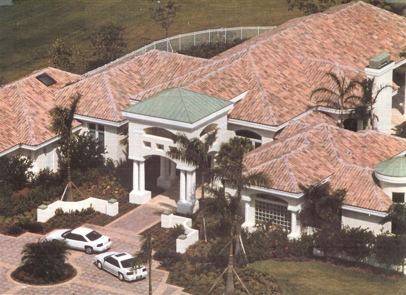 Upscale, sprawling house with red tile roof, white exterior, and palm trees. Two cars parked in front.