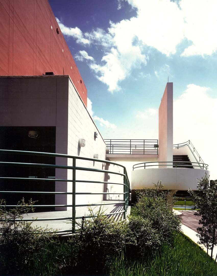Exterior view of a building with a red wall, accessible pathway, and green railing on a sunny day.