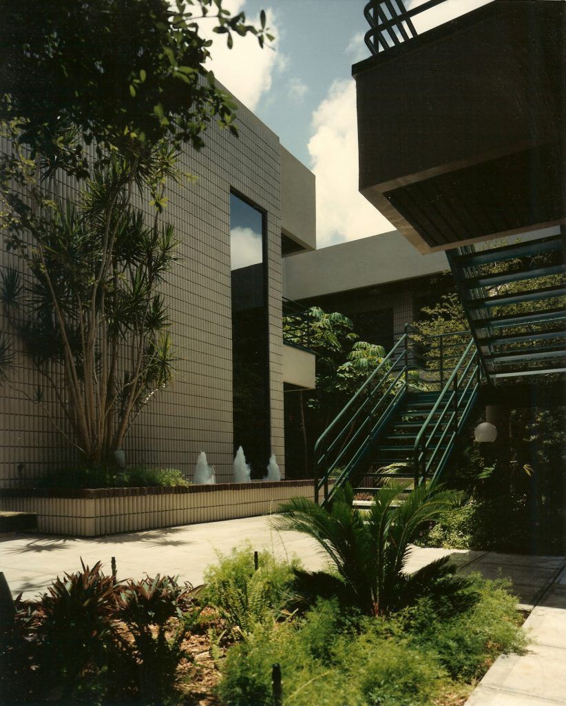 Exterior view of modern buildings with stairs, landscaping, and a fountain. Sunny day.