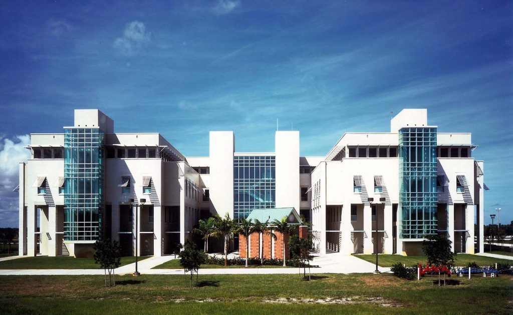 Modern building with white facade and glass accents under a blue sky, grass lawn in foreground.