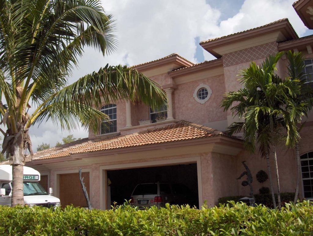 Two-story house with terracotta roof, garage door open, palm trees, and a van parked nearby.
