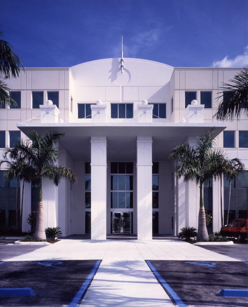 White office building with columns, arched doorway, and palm trees.