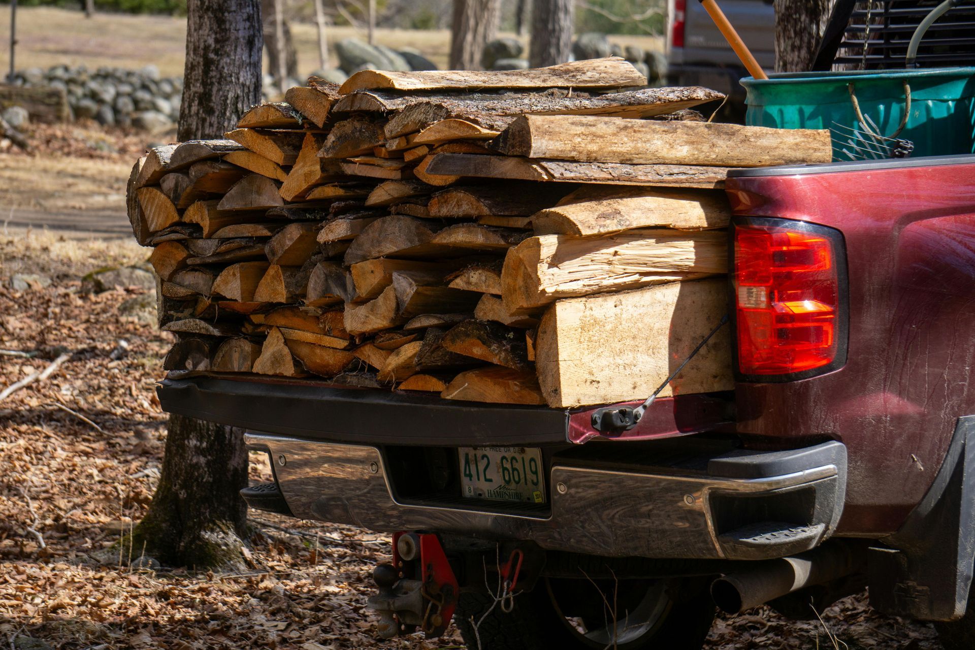 Pickup truck bed loaded with stacked firewood in a wooded outdoor area
